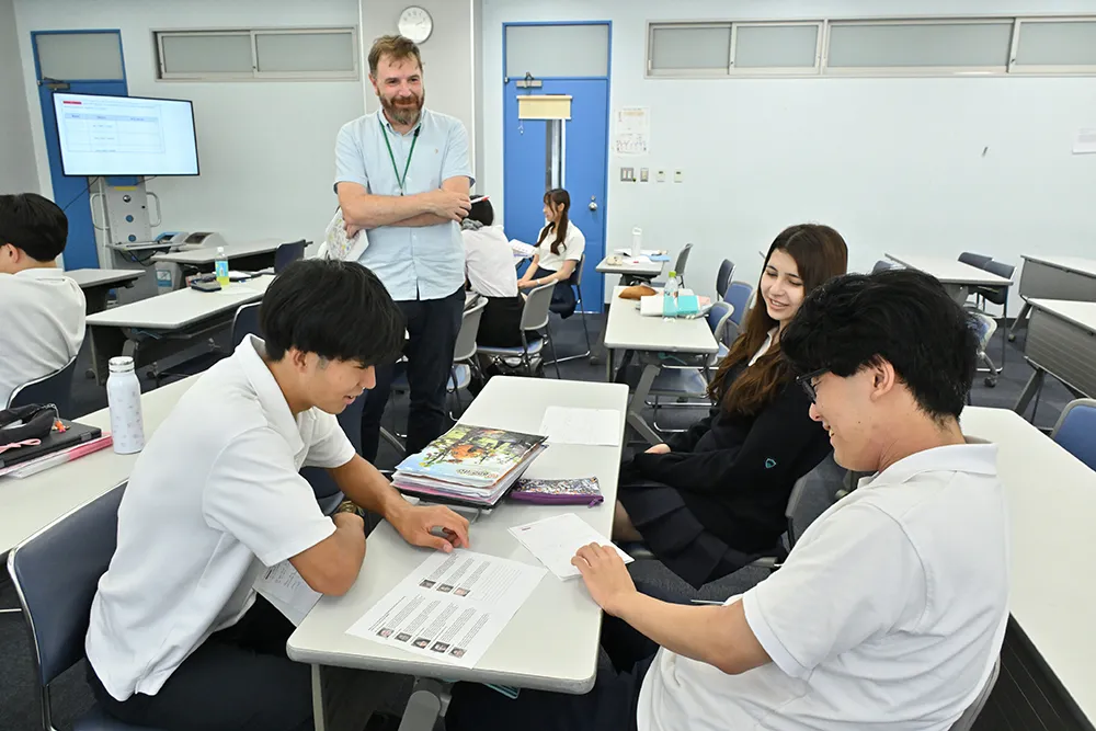 自分で考えたことを英語でお互いに伝え合う生徒たちと、その様子を楽しそうに見守るベリー先生